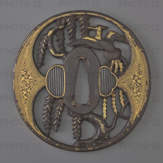 Crossguard tsuba, Japanese, Edo period 1603–1868, early 18th century, weapons — katana crossguard tsuba, maru gata round, kaku mimi rectangular edge, ryôhitsu-ana oval blinded with shakudô. Decorated in positive openwork yô sukashi with a hoo phoenix perched on a willow tree; decoration and edge have gold inlay using the nunome technique. Aizu-Shôami style. Not signed. Dimensions: height 8.4 cm, width 8.2 cm, depth 0.45 cm., A round dark metal object with a central oval opening and an irregular cutout, decorated with areas of gold detailing; a stylized bird with outstretched wings appears near the top right, and a group of hanging, leaf-like forms dangles toward the lower left and center; two rounded, ribbed panels flank the central opening and are outlined in gold; ornate, fan-shaped gold patterns fill the left and right edges of the circle; the surface shows textured, carved branches and organic shapes, with a color palette of dark brown or black metal and bright gold accents against...
