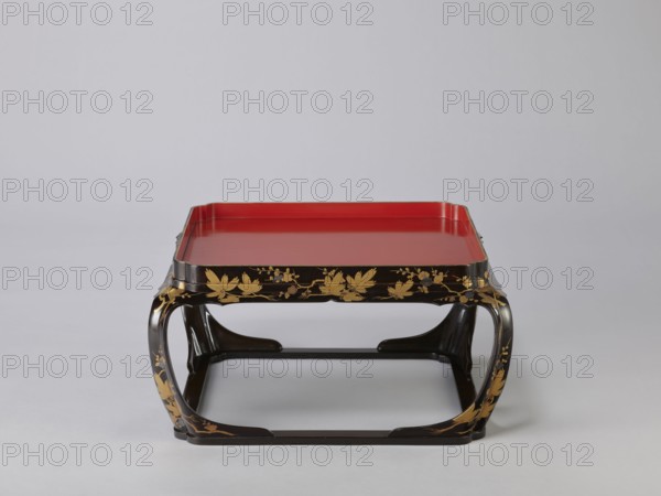 Tray on legs kakeban, gift; Japanese, Edo period early 19th century. One of a set of three tables placed one on top of the other; almost square red top with high edges and bow legs connected at the bottom by a square frame forming the base. Sides and legs covered with black lacquer and sprinkled with gold using the maki-e technique with flowering cherry, plum trees, pine branches, flowers, twigs — winter motifs. Piece of furniture. Height 25.3 cm; width 47.5 cm; depth 46.0 cm., A low rectangular tray-like table with a glossy red top set in a dark frame decorated with gold leaf and floral motifs, the frame forming curved open sides and a rectangular base, visible colors include red, black, gold, and a neutral gray background.