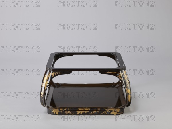 Tray on legs kakeban, one of a set of three tables placed one on top of the other; almost square red top with high edges and bow legs connected at the bottom by a square frame forming the base. Sides and legs covered with black lacquer and sprinkled with gold using the maki-e technique with flowering cherry and pine branches. Early 19th century Edo period, Japan. Piece of furniture. Height 25.3 cm; width 47.5 cm; depth 46.0 cm., A low, rectangular stand with curved legs and a recessed tray, finished in dark brown or black lacquer with gold floral and leaf ornamentation along the legs and base; the stand has an open top frame and a glossy interior surface, set against a plain light gray background.