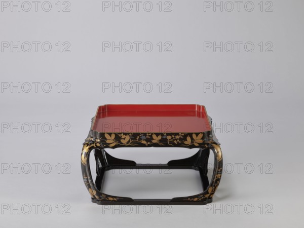 Tray on legs kakeban, gift, Japanese, Edo 1603–1868, early 19th century. One of a set of three tables placed one on top of the other; almost square red tops with high edges and bow legs connected at the bottom by a square frame forming the base. Sides and legs covered with black lacquer and decorated with gold powder using the maki-e technique in a motif of blooming plum and pine branches plum trees, flowers, trees, pines, twigs, winter. Piece of furniture. Height 22.0 cm; width 41.5 cm; depth 40.0 cm., A low rectangular tray with raised edges in red sits atop a black curved stand decorated with gold floral and leaf motifs, the stand showing several sweeping arch shapes and smooth glossy surfaces in black, red, and gold against a pale gray background.