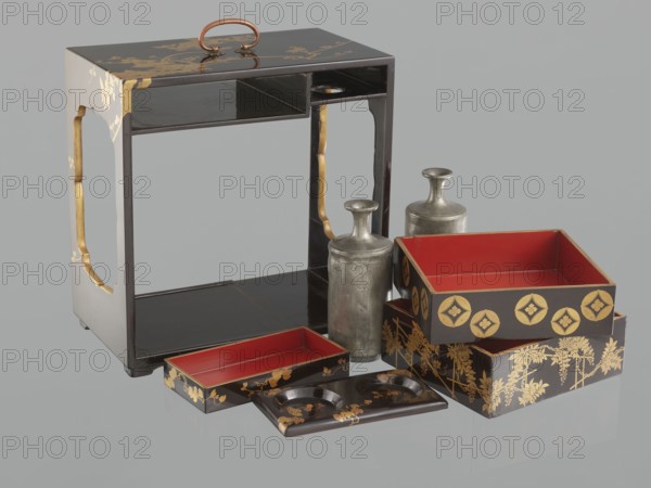 Portable picnic set sagejûbako, Japanese, Edo 1603–1868–Meiji 1868–1912, 19th century. Rectangular cabinet without side walls on a stand; two food containers stacked on the stand set incomplete; originally four; two tin sake bottles on a stand beside the containers. Top tabletop has a handle, one small drawer, and a shelf for trays trays missing. Exterior covered with black roiro-nuri lacquer; interiors of food containers covered with vermilion lacquer. Surface ornament executed in hiramaki-e and nashiji techniques, depicting blooming wisteria, camellias, plum trees, wolfberries, mon, leaves, and rosettes coins. Such portable eating sets were called in Japan kôchô, sagejû, hanami bentô and were popular from the Momoyama period mid-16th–early 17th century and in the 18th–19th centuries. Item; height 31.3 cm, width 30.5 cm, depth 17.8 cm, weight 2.29 kg., A small lacquered wooden stand with a handle on top sits beside a group of decorative boxes and two metal bottles; the stand is dark b...