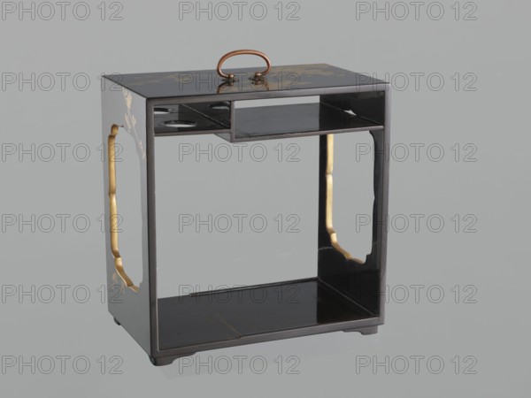 Portable picnic set sagejûbako, Rectangular cabinet without side walls on a stand with two stacked food containers set incomplete; originally four; beside them on the stand are two tin sake bottles. Top tabletop has a handle, one small drawer, and a shelf for trays missing. Entire exterior covered with black roiro-nuri lacquer; interiors of food containers with vermilion lacquer. Surface ornament executed in hiramaki-e and nashiji techniques, depicting blooming wisteria, camellias, and rosettes/coins; also motifs of leaves, plum trees, and wolfberries; includes mon. Such portable eating sets were called in Japan kôchû, sagejû, hanami bentô and were popular from the Momoyama period mid-16th–early 17th c. and in the 18th–19th centuries. 19th century Edo–Meiji periods, Japan. Height 31.3 cm; width 30.5 cm; depth 17.8 cm; weight 2.29 kg., A small rectangular wooden stand with a glossy black finish and a rounded brass handle on top; the stand has an open central compartment with a raised sh...