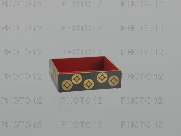 Portable picnic set sagejûbako, Rectangular cabinet without side walls. On a stand there are two food containers stacked on top of each other set incomplete; originally four; next to the containers on the stand are two tin sake bottles. The top tabletop, equipped with a handle, has one small drawer and a shelf for trays missing. Entire surface covered with black roiro-nuri lacquer; interiors of the food containers covered with vermilion lacquer. Ornament executed in hiramaki-e and nashiji techniques depicting blooming wisteria, camellias, rosettes coins, mon, leaves, plum trees, and wolfberries. Such portable eating sets were called variously in Japan kocho, sageju, hanami bento and were popular from the Momoyama period mid-16th–early 17th century, and in the 18th and 19th centuries. 19th century Edo–Meiji periods, Japan. Dimensions: height 31.3 cm, width 30.5 cm, depth 17.8 cm; weight 2.29 kg., A shallow rectangular box with an open top sits on a reflective surface; the interior is re...