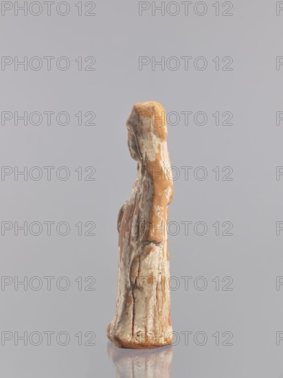 Standing woman figure — tomb figurine, Chinese, ceramics, female figurine, Tang dynasty 618–907, early 10th century, China; sculpture, height 19.3 cm, A small upright figurine with a weathered surface stands against a plain background, showing a mix of tan, beige, off-white, and hints of reddish-brown colors; the form suggests a draped figure with a rounded head and elongated body, surface irregularities and flaking paint reveal layered coloration, and the base sits on a reflective surface that mirrors muted tones.