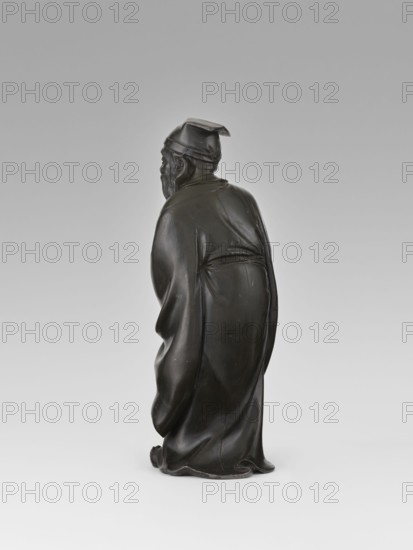 Sage, unknown sculptor, figurine, Chinese art, Chinese culture, fan, man, scholar, Qing dynasty 1644–1911, long flowing robe, cap on the sage's head, 19th century, China, sculpture, height 28.0 cm, A dark brown sculpted figure of a robed person seen from behind, wearing a square cap and a long flowing robe with visible folds and drapery, with a beard and hair visible at the side of the head; the surface has a smooth, polished finish with subtle highlights and a few lighter wear spots, and the background is a gradient of light gray to off-white.
