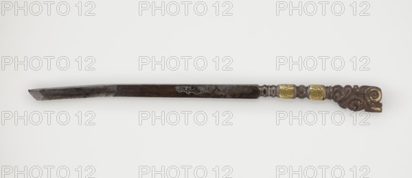 Dagger, 19th century, Tibetan, militaria; dagger weapon, height 25.8 cm., An elongated metal object lies horizontally against a light background, showing a dark, weathered blade with irregular patina and a beveled tip on the left, transitioning toward a more decorative right end that features a carved handle with swirling, organic shapes and a carved hole, flanked by a pair of raised, faceted bands with a golden color and a short section of rounded ornamental metalwork between them; visible colors include dark brown, black, gold, and the light neutral background.