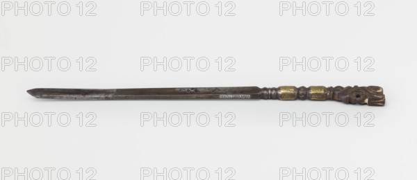 Dagger, 19th century, Tibetan; craft militaria weapon dagger, height 25.8 cm., A long narrow object with a dark metallic blade that tapers to a pointed end and shows patches of darker and lighter gray, a few subtle engraved marks along the blade, and a carved handle featuring a dark brown material with decorative shapes and a few gold-colored bands; the background is white and light gray.