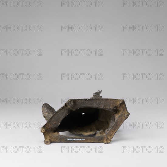 Buddhist deity on a buffalo, on a base;,  noted; figurine; Chinese; lotus iconography; Chinese Buddhism; Qing dynasty 1644–1911, 19th century; buffaloes; Buddhist art; sculpture; height 35.5 cm, width 21.5 cm, A worn hollow object rests on a flat surface against a light gray background, appearing dark brown with areas of lighter brown and ochre; the object has an irregular, roughly rectangular opening facing the viewer, with rough, uneven edges and a textured, pitted surface; a protrusion extends from one side and a small, irregular fragment rises from the top, both sharing the same brown and ochre tones; inside the opening the interior appears dark with patches of lighter brown, and the base beneath the opening shows a small strip of a different hue.