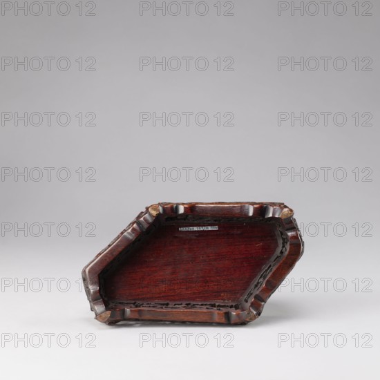 Buddhist deity on a buffalo on a base; figurine; Chinese; Chinese Buddhism; lotus iconography; Qing dynasty 1644–1911, 19th century; sculpture; height 35.5 cm, width 21.5 cm., A wooden tray or shallow box with a faceted, irregular hexagonal shape sits on a light surface against a pale gray background; the object has a polished deep reddish-brown wood tone with darker grain visible on the flat interior, a carved raised rim with scalloped edges, and areas of darker brown along the carved details and corners.