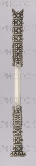 Hookah mouthpiece; maker, Islamic art; Arabic; smoking accessory hookah/pipe; geometric ornament and pearling; early 20th century; likely Yemen or Arabia Petraea origin; length 18.1 cm; diameter 2.1 cm., A vertical metallic object with an elongated central shaft in a pale silver color and decorative end sections in a darker silver tone; the top end features a crown-like cluster of rounded beads and faceted diamond-shaped elements, surrounded by coiled wire and rows of small spherical beads, with textured raised bands and looped metal details; the lower end mirrors the top with similar patterned bands of coiled wire, clusters of small round beads, and diamond-shaped facets culminating in a rounded base with a ring of larger beads; the central shaft is smooth and reflective, showing subtle linear facets and a uniform pale silver finish against a light muted background in a very light grayish-lavender tone.