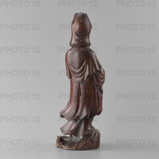 Guanyin Bodhisattva, Qing dynasty 1644–1911, 19th century, China; sculpture figurine of Chinese Buddhism depicting the goddess Guanyin; height 31.6 cm, width 11.5 cm, depth 9.5 cm; Chinese art, Chinese culture., A carved wooden statue shown from the back, displaying smooth, flowing drapery and layered robes with rounded folds; the figure stands on an irregular carved base that has textured, organic detailing. The surface of the statue is a rich dark brown with areas of lighter brown highlights and a subtle sheen. The background is a flat, light gray.