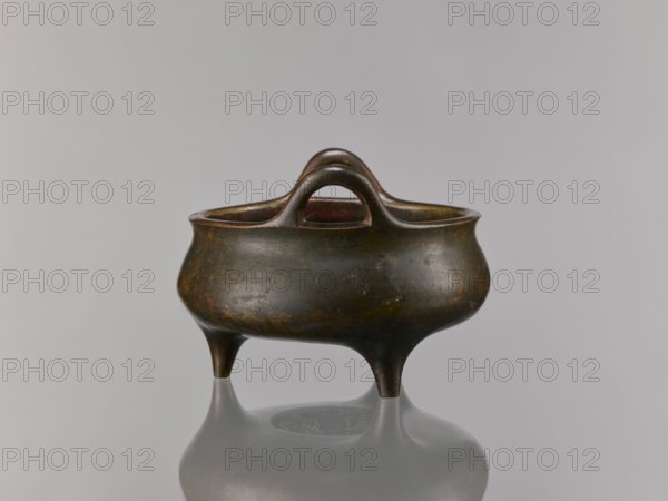 Li-type incense burner, incense burner in bronze, Chinese ceremonial vessel with dragon iconography, Qing dynasty 1644–1911, 18th–19th century, China; height 13.5 cm, width 18.6 cm., A low, rounded three-legged metal vessel with a dark brown and greenish patina, showing areas of worn bronze and subtle reddish-brown tones inside the rim, with a curved double-arched handle rising from the lip and a smooth reflective surface beneath that mirrors the vessel.