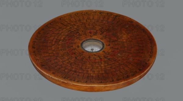 Feng shui compass luopan, security provenance, navigational object, Chinese art, Chinese culture, Qing dynasty 1644–1911, calendars, clocks, Zodiac Chinese, 19th century, China, Huizhou, measuring instrument, diameter 13.8 cm, A round wooden disc with a smooth, glossy finish sits against a plain gray background, showing a central circular indentation with a small metallic dish that has a reflective, slightly tarnished surface; the top of the disc is covered with concentric engraved or painted markings and small decorative strokes in dark and muted red tones, and the wood itself displays warm brown and amber hues with subtle grain patterns and a few small worn spots along the edge.