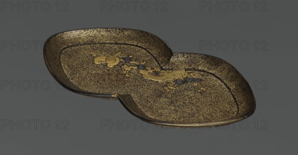 Tray, lacquerware, Japanese, Edo period 1603–1868, 1st half of the 19th century. Decoration: asymmetrical composition of an old plum tree trunk with young shoots; motif includes plum trees and birds kachôga. Vessel; height 2.6 cm, width 17.8 cm, depth 9.5 cm., A shallow, double-lobed tray with a textured speckled surface in gold and dark brown, featuring a raised rim and an ornate central motif with stylized floral and organic shapes in gold and dark gray; the background is a flat medium gray.
