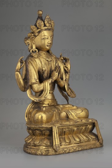Four-armed Bodhisattva Avalokiteshvara Chaturbhuja, The bodhisattva is shown in one of his tantric forms called shadakshari. Single-headed, four-armed figure seated in meditative pose on a lotus throne. One pair of hands in namaskara mudra; the other holds a lotus flower and a rosary almost unpreserved apart from one element. Dressed in bodhisattva regalia: crown, earrings, necklace, inlaid bracelets on wrists and ankles, a sash flowing from shoulders to forearms, an antelope skin draped over the left shoulder, and a foot-long band with floral pattern around the lower body. A coiffed knot of hair atop his head is crowned by the head of Amitabha. The plaque closing the base is missing. Sculpture, 2nd half of the 18th century, China/Tibet Sino-Tibetan/Himalayan style and Chinese influence. Height 22.5 cm, width 14.5 cm, depth 9.5 cm. Materials: not specified., A gilded seated figure on a decorative base, rendered in gold tones with visible darker patina in places, wearing an ornate crown...