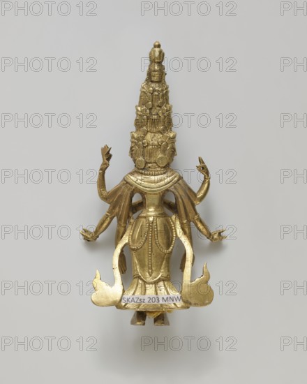 Guanyin, figurine, Chinese/Tibetan, bodhisattva iconography, heads, flames, hands, 19th century, sculpture; height 9.9 cm, width 5.2 cm, depth 2.0 cm, A small metallic sculpture of a standing humanlike figure with an elongated, tiered headdress and multiple arms, rendered in a gold color against a light gray background, showing ornate decorative details on the headdress and torso, with flowing drapery elements and stylized flamelike shapes at the base.
