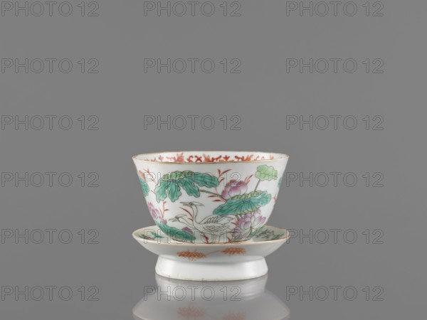Bowl with stand, ceramics. Colored porcelain bowl decorated with lotuses; stand decorated inside with an ornamental band. On the obverse of the stand are a bird and flowered branches; on the reverse are bamboo shoots and cranes. Guangxu style, Qing dynasty 1644–1911, 19th–20th century Guangxu era, 1875–1908. Chinese vessel. Height 8.5 cm; diameter 10.6 cm., A small white porcelain cup with a matching saucer sits against a gray background; the cup is decorated with green leaves, pink and purple flowers, and orange accents, and the saucer shows similar green and orange decorative motifs, with a subtle reflection visible beneath them.