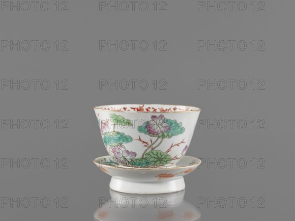 Bowl with stand, ceramics; decorated colored porcelain in Guangxu/Qing style Qing dynasty, 1644–1911, 19th–20th century Guangxu era, 1875–1908. Decorated inside with an ornamental band. On the obverse of the stand are a bird and flowered branches; on the reverse are bamboo shoots. Motifs include lotuses, cranes, and bamboos. Chinese; vessel. Height 8.5 cm; diameter 10.6 cm., A white porcelain cup and matching saucer sit on a reflective surface against a gray background; the cup has a flared rim and the saucer has a shallow curved center, both decorated with painted floral motifs in green and pink with accents of reddish-orange and touches of gold along the rim and on some design elements.