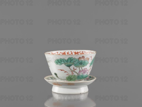 Bowl with stand, ceramics;, Colored porcelain, decorated inside with an ornamental band. On the obverse of the stand are a bird and flowered branches; on the reverse are bamboo shoots. Motifs: lotuses, cranes, bamboos. Style/period: Qing dynasty Guangxu era, 19th–20th century 1875–1908. Function: vessel. Dimensions: height 8.5 cm; diameter 10.6 cm. Chinese., A small porcelain cup and matching saucer sit against a neutral gray background, the cup showing a flared rim and the saucer a slightly raised center; both pieces are predominantly white with painted botanical motifs featuring green leaves, pink flower petals, and touches of brownish-orange in the floral accents and rim detailing, with fine darker outlines and delicate shading on the painted foliage and blooms.
