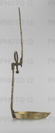 Oil lamp, Islamic art, Persian, oil lamp for lighting decorated with birds, geometric motifs, palmettes; lamp with a side decorative shaft, stylized medallion, palmette finial. 19th–20th century, Central Asia and/or Iran; height 45.5 cm, diameter 15.5 cm., A metallic object with a long thin vertical arm that has an uneven, textured surface and a looped handle near its midsection, attached to a horizontal bracket and a short peg ending in a rounded knob, connected at the base to a shallow, oval dish with a small pointed spout; the object is primarily brass-colored with areas of darker patina and faint greenish and brownish tones, set against a plain light gray background.