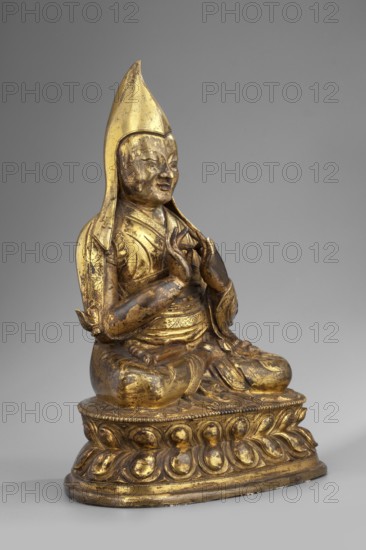 Gelukpa teacher, unknown sculptor; Tibetan Buddhist art, Himalayan; mudras, lotus throne, headgear; 18th century, Tibet; sculpture; height 22.5 cm, width 16.5 cm, A gilded statue of a seated figure on a rounded lotus base, shown against a plain gray background, with a tall pointed headdress and draped robes; the figure's hands are raised and held together in a gesture, the face has a serene expression, and the surface shows areas of worn gold revealing darker underlying tones; visible colors include gold, dark brown, and gray.