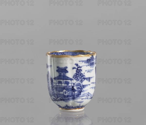 Cup, ceramics, blue-and-white porcelain; Qing dynasty, 19th century Qing, 1644–1912; Chinese; vessel with landscape motifs; part of a 22-piece tea and coffee set including a teapot, 6 cups, 6 saucers, a bowl, a cover, and a plate; height 6.5 cm, width 5.9 cm, diameter 5.9 cm., A small porcelain cup with a scalloped rim edged in gold sits against a plain gray background, decorated in blue and white with a detailed landscape scene including a pagoda-like building, trees, and architectural elements; the interior shows blue patterning and the base also has a gold trim, and the cup casts a soft reflection on the surface below.