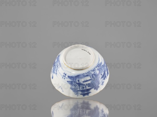 Teapot, ceramics; blue-and-white porcelain teapot with landscape motifs; part of a 22-piece tea and coffee service includes teapot, 6 cups, 6 goblets, 6 saucers, a bowl, a cover, and a plate; Qing dynasty, 19th century 1644–1912; Chinese; vessel; height 7 cm, diameter 14.3 cm., An upside-down ceramic bowl with blue painted decorative patterns rests on a reflective surface against a plain gray background, showing white and blue colors on the bowl with a visible unglazed circular base rim in a light beige tone and the reflection beneath mirroring the bowl's blue and white design.