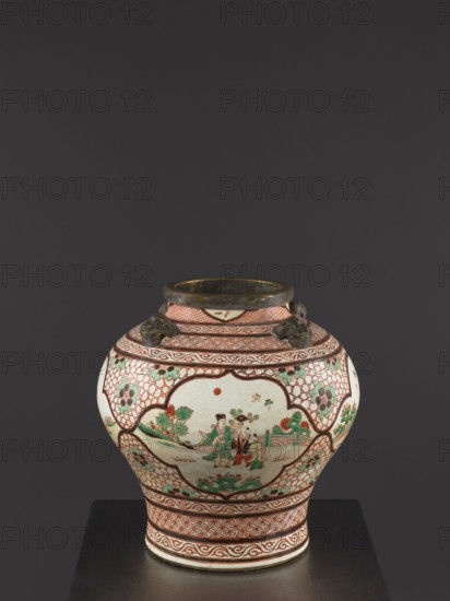 Vase, mid-18th century Qing dynasty, 1644–1911, China. Colored porcelain decorative vessel, height 40.5 cm, diameter 40 cm. Mascarons on the shoulder; decoration: four reserves with figural representations; gilded edge., A rounded ceramic jar with a narrow neck and flared rim sits against a dark gray background on a black surface; the jar has a predominantly white base with decorative patterns in red and green, with additional accents in brown and black. The body features several framed panels bordered in red lattice and wave motifs, with floral designs in green and red in the lattice areas. One main panel shows a scene with a group of figures and surrounding landscape elements rendered in green and red on the white background. The neck and shoulder have banded geometric and scroll patterns in red, and there are small sculpted handles on the shoulder in a dark brownish color. The rim appears darker brown with some worn areas.