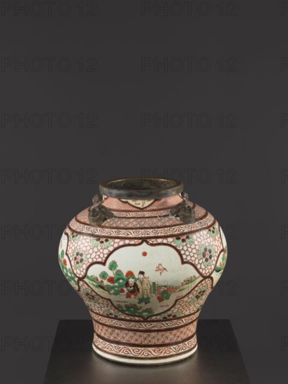 Vase., Colored porcelain with gilded edge. Mascarons on the shoulder; decoration: four reserves with figural representations. Mid-18th century Qing dynasty, 1644–1911, China. Height 40.5 cm; diameter 40 cm. Chinese art; decorative vessel; mascarons; figural scenes., A rounded ceramic jar with a narrow neck sits on a dark surface against a dark gray background; the jar is predominantly white with red, green, and black decorative patterns and painted scenes, featuring red geometric borders and latticework, green floral motifs, and a central painted scene with human figures and plants; the rim and three small sculpted handles at the neck appear dark metallic or bronze in color; overall colors visible include white, red, green, black, and bronze.