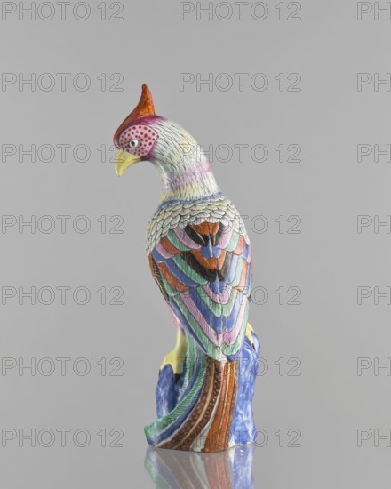 Rooster figurine, Chinese, Qing dynasty 1644–1911, 19th century; colored porcelain ceramics; sculpture depicting a rooster with rocks; animals/birds iconography; height 28.5 cm, width 14.5 cm., A colorful ceramic bird figurine perched on a textured ceramic base, shown from the back and slightly turned to the side; the bird has a red crest, a yellow beak, and a head with pale tones and dotted markings, while its body is covered in layered, scalloped feathers painted in a palette of green, blue, pink, purple, orange, brown, black, and white, with the base displaying blue and brown tones and a glossy finish, all set against a plain gray background.