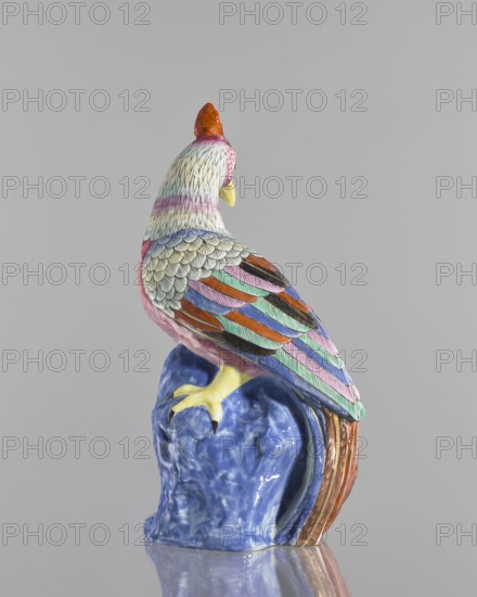 Rooster figurine, Chinese, Qing 1644–1911, 19th century; colored porcelain sculpture of a rooster animal figurine/bird with rocks; height 28.5 cm, width 14.0 cm., A colorful ceramic bird perched on a glossy blue base, shown from behind and slightly to the side, with a curved neck and a small crest. The bird's feathers are painted in a mix of pastel and bright colors including pink, mint green, light blue, orange, purple, black, yellow, and white, with detailed scale-like feather patterns on the upper back and layered elongated feathers on the wings and tail. The beak and feet are yellow, and the base has a marbled blue surface with glossy reflections. The background is a smooth neutral gray.