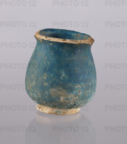 Jug, Abdullazad Mirza Baba fl. ante 1939, Islamic art, Persian, Ilkhanids 1256–1335, ceramics, cups, vases, everyday life in the Middle East, 13th–14th century, Iran, vessel, weight 0.378 kg, height 12.5 cm, diameter 11.5 cm, A small rounded vessel sits against a pale background, its surface predominantly blue with areas of lighter and darker blue and patches of muted greenish-blue and beige where the finish is worn. The rim and base show exposed beige material with rough, chipped edges. The vessel has an uneven, slightly bulbous shape with a narrow top opening and a textured, weathered surface. A soft reflection of the vessel appears on the smooth surface beneath it.