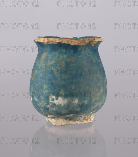 Jug, Abdullazad Mirza Baba fl. ante 1939, Ilkhanid Persian ceramic vessel cup/vase, 13th–14th century Iran, Islamic art; everyday-life object; height 12.5 cm, diameter 11.5 cm, weight 0.378 kg., A single rounded vessel with a flared rim sits centered against a plain pale background, the vessel showing a textured surface in shades of blue and turquoise with areas of lighter bluish-white and small mottled spots, and a worn, sandy-beige rim and base with visible rough edges.