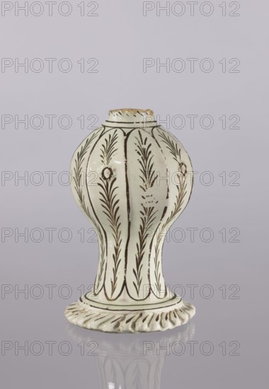 Bottle, Persian, Qajar dynasty 1785–1925, glazed ceramic vessel bottle, 19th century, Iran; ceramics with decoration in bronze lines and stylized feathery twigs; diagonally knobbed foot edge; height 19.0 cm, width 12.0 cm., A ceramic vessel with an elongated bulbous body and a flared, ridged base sits against a pale lavender-gray background; the vessel is predominantly off-white with dark brown linear and botanical painted decoration forming vertical panels of leafy motifs and small circular rosette-like accents, the rim shows areas of exposed clay in a tan color, and the glossy surface creates a subtle reflection of the object on the smooth surface beneath.