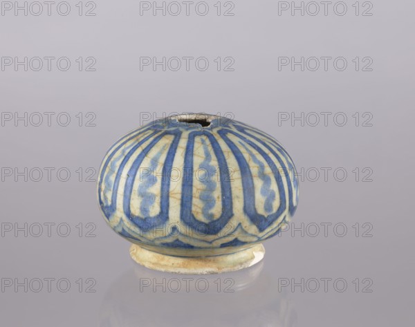 Bottle belly, purchase provenance Abdullazad Mirza Baba fl. ante 1939, Islamic art, Persian, glazed ceramics, utility ceramic bottle decorated with cicadas, 18th century Iran, vessel, height 10.2 cm, diameter 14.1 cm, A rounded ceramic object with a flattened top and a small irregular opening, sitting on a short circular foot, decorated with vertical elongated petal-like motifs in blue on a cream background with visible hairline cracks and areas of discoloration, showing shades of blue, cream, beige, and a hint of brown, photographed against a smooth pale grey-lavender backdrop with a soft reflection beneath the object.