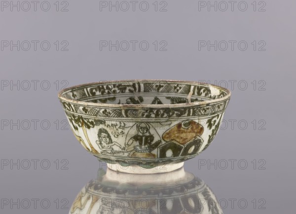 Bowl, late 19th century 1893, Iran. Ceramic vessel, height 8.5 cm, diameter 19 cm. Persian/Qajar dynasty. Decoration on the rim: Rostam, with a dragon and Majnun i Lejla and the date 1893. Figural scenes, dragons, birds, literary motifs; utility tableware bowl. Cultural context: Persian/Islamic art., A shallow ceramic bowl with painted decoration sits on a reflective surface, showing a group of human figures and abstract shapes around its exterior; the bowl is primarily white with painted areas in dark green and brown, with touches of yellowish-brown and black, and a rim that shows some wear.