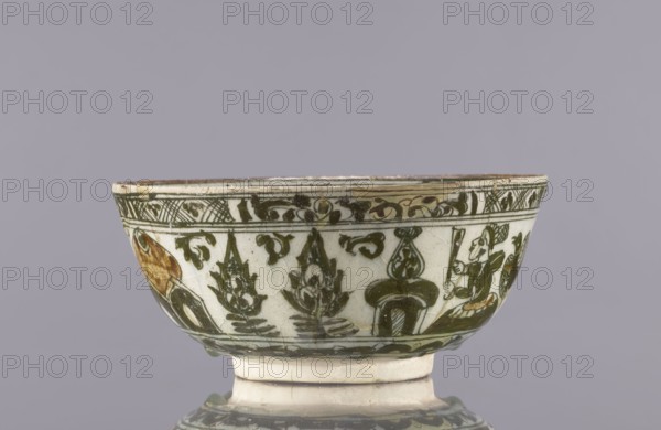 Bowl, late 19th century, Iran. Ceramic vessel, height 8.5 cm, diameter 19 cm. Decoration on the rim: Rostam, with a dragon and Majnun i Lejla and the date 1893. Persian, Qajar dynasty 1785–1925. Figural scenes, literary motifs; imagery includes dragons and birds. Function: tableware/utility ceramic., A shallow ceramic bowl with a flared rim and a short foot rests against a plain mauve-gray background; the bowl's surface is primarily off-white with green painted decorative motifs including stylized plant forms and scrolling patterns, and there are areas of brownish-orange pigment on parts of the decoration; the rim shows a narrow band of darker green ornament and the lower body repeats green motifs above a green horizontal border, while the foot is off-white with some signs of wear.