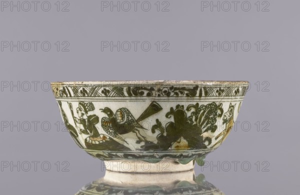 Bowl, Abdullazad Mirza Baba fl. ante 1939, Islamic art, Persian art, Persian culture, Qajar dynasty 1785–1925, ceramics, tableware, utility ceramics, lutes musical instruments, figural scenes, jambiyah, bowls, dragons iconography, literary motifs, birds. Decoration on the rims: Rostam, with a dragon and Majnun i Lejla and the date 1893. Late 19th century, Iran. Vessel; height 8.5 cm, diameter 19 cm., A shallow ceramic bowl with a flared rim sits against a plain gray background; the bowl has a pale off-white base color with dark green painted decoration around its exterior showing stylized foliage, a bird with patterned wings, and curved ornamental motifs, with a darker green band near the rim featuring a repeating decorative border; there are areas of brownish discoloration and glaze drips along the lower edge, and the bowl rests on a short foot that is off-white with subtle green glaze accents.