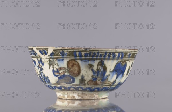 Bowl, Abdullazad Mirza Baba fl. ante 1939, Islamic art, Persian, Qajar dynasty 1785–1925, ceramics decorated with gazelles, figural scenes, lions, female figures; rim decoration: figure with nargile, other figures, lion, palmettes, architecture, inscriptions. 2nd half of the 19th century, Iran. Vessel; height 9 cm, diameter 20 cm., A ceramic bowl with painted decoration sits against a plain light gray background; the bowl shows a band of painted figures and motifs in shades of blue, brown, green, and off-white, with visible glazing and areas of wear and small chips along the rim and body; a few humanlike figures are depicted in blue and brown tones seated on patterned surfaces, accompanied by decorative floral or foliate elements in blue and green; the lower section and foot of the bowl show a mottled off-white and brown surface with glaze variations and some roughened spots.
