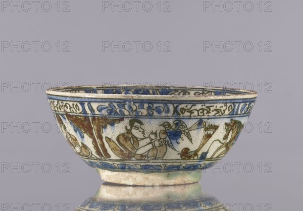 Bowl, Abdullazad Mirza Baba fl. ante 1939, Qajar dynasty 1785–1925, 2nd half of the 19th century, Iran. Glazed ceramic vessel tableware, height 7.5 cm, diameter 17.4 cm. Decoration: knightly and figurative scenes with horses and falcons; rims decorated with figures, architecture, flowers, animals, palmettes, and inscriptions. Persian/Islamic art; ceramics., A shallow ceramic bowl with a rounded foot, shown against a plain light gray background, featuring painted decorative bands and figural scenes around its exterior in colors including blue, green, brown, and cream; the rim and upper band display blue floral and scroll motifs, while the main body shows a group of stylized human figures and animals rendered in brown and green outlines with blue accents, and the lower portion has a repeated blue petal-like border above the foot.