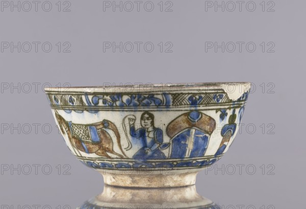 Bowl, maker, 2nd half of the 19th century; Qajar dynasty 1785–1925, Iran; ceramic vessel, height 8 cm, diameter 17.5 cm; Persian Islamic art; used for tea; decorated with figural scenes including female images and archers, figures on the rims, architecture and animals; provenance includes Abdullazad Mirza Baba fl. ante 1939., A ceramic bowl rimmed with decorative bands shows painted figurative scenes in blue, brown, green, and white; the rim has a patterned border with floral motifs in blue and green, below which a scene includes a personlike figure in blue holding a long curved object between two stylized animals or objects rendered in brown and blue, with additional ornamental elements and a chipped area at the rim revealing bare ceramic.