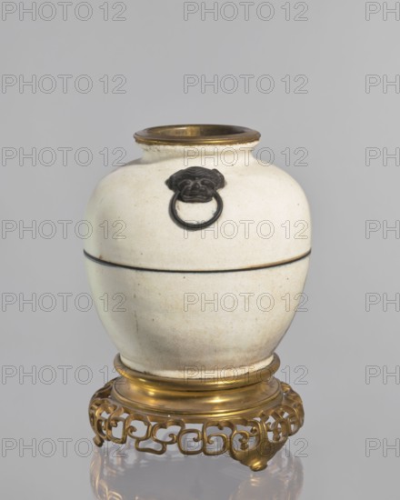 Gilded bronze mounted vase — lamp body; maker, Chinese; Qing dynasty 1644–1911; decorative vessel; vase/lamp; cracklework decoration; 18th century, China; vessel; height 33 cm, A rounded ceramic jar with a crackled off-white surface sits on an ornate metal stand; the jar has a short neck with a metallic rim in a warm gold tone and a thin dark horizontal band around its midsection, and a dark decorative ring held in a sculpted dark element attached near the neck; the stand beneath is an intricate openwork design in a shiny gold color, and the background is a uniform light gray.
