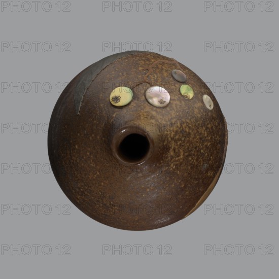 Sake bottle tokkuri, gift; Japanese art; Edo 1603–1868–Meiji 1868–1912; bottle for sake; A bottle with a spherical belly and a narrow cylindrical neck; covered with brown glaze which in the upper part of the belly and on the neck turns light coffee-coloured and becomes spotted. Decorated on the belly with a branch of biwa Japanese medlar, fruits made with green-yellow glaze and inlaid with mother-of-pearl, leaves made using the technique of sprinkling on black lacquer. 19th century, Japan, Bizen; vessel; height 18 cm, diameter 11.8 cm., A round, bulbous ceramic vessel viewed from above with a central round opening, showing a textured surface in shades of brown and rust with speckled darker brown areas; a few small round decorative discs in pale green, iridescent pearly white, and muted yellow are arranged near the top edge, and there is a dark, rough patch of material or repair on one side; the background is a flat gray.