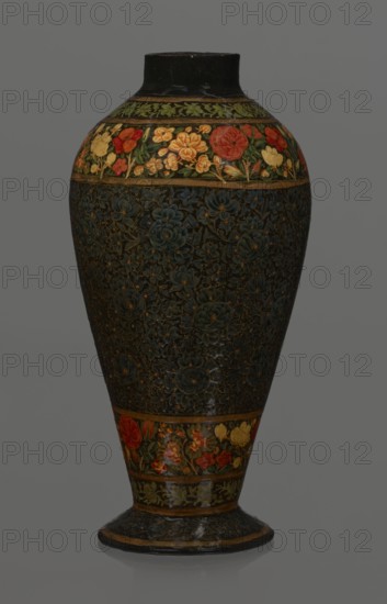 Vase, Qajar dynasty 1785–1925, Islamic Persian floral ornament. Lacquer vase, 19th century, Iran. Decoration: densely placed plant motifs peonies with gold contouring; on the collar and above the foot flowers red and gold. Vessel, height 32.0 cm, diameter 17.0 cm., A tall, urn-shaped ceramic vase with a narrow neck and flared foot, predominantly dark in color with intricate carved or painted floral patterns covering most of its body; a decorative band near the top features a colorful floral motif with reds, yellows, greens, and touches of orange set against a darker background, and a similar colorful band appears near the base; the central body shows dense, textured floral designs in deep bluish-green and dark tones with subtle golden accents; the neck and foot have dark brown to black areas with hints of worn lighter brown.