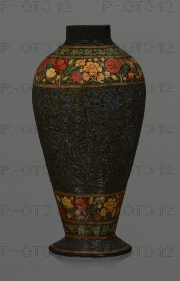 Vase, Qajar dynasty 1785–1925, Persian, Islamic art; lacquer vase, 19th century, Iran; vessel, height 32.0 cm, diameter 17.0 cm; decoration: densely placed plant motifs peonies with gold contouring; on the collar and above the foot flowers red and gold., A tall, rounded vase with a narrow neck and flaring base sits against a plain gray background; its surface features dense floral patterns with a dark, almost black background on the main body and bands of colorful flower decorations near the top and base. The decorative bands show a mix of red, orange, yellow, green and hints of lighter tones forming stylized blossoms and leaves, while the central dark area is filled with intricate raised floral motifs in deep blue and muted gold outlines. The neck and base edges are darker, appearing black with worn highlights, and the lower flaring foot echoes the dark floral texture with thin gold bands.