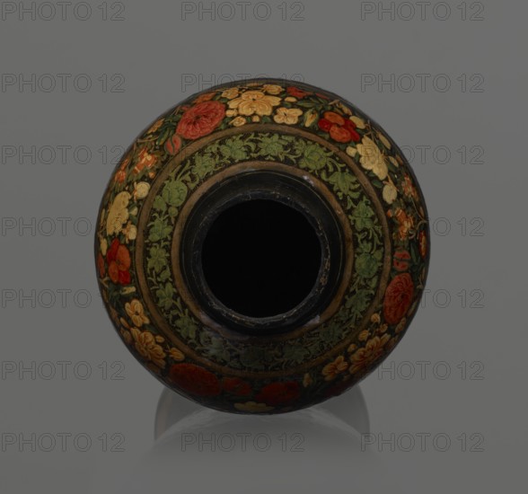 Vase, Qajar dynasty 1785–1925, Islamic art, Persian; lacquered vessel, 19th century, Iran; height 32.0 cm, diameter 17.0 cm. Decoration: densely placed plant motifs peonies with gold contouring; collar and above the foot decorated with flowers red and gold. Inside a card no. 54 with an inscription in Italian identifying it as a lacquer vase., A round decorative object viewed from above with a central dark opening, featuring concentric bands of floral patterns in green, red, orange, yellow, and gold on a black background, with a subtle reflection beneath it and a plain gray background.