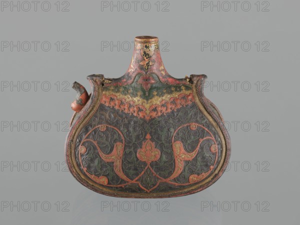 Waterskin matara, 2nd half of the 16th century, Turkey; vessel, leather, height 23.0 cm, width 24.5 cm, depth 14.0 cm, weight 0.62 kg. Kidney-shaped waterskin with rounded bottom, narrow neck and small spout for drinking, decorated with appliqué arabesques cut from shagreen and arabesques painted with gold; features a protective emblem in the form of a six-pointed star Seal of Solomon intended to ensure the water's freshness. The leather matara imitates luxury gold bottles set with precious stones used at the sultan's court and may have been used by the sultan during military expeditions. Only four such leather mataras are known worldwide., An ornate decorative vessel with a rounded, flattened body and a short neck, shown against a plain gray background; the vessel displays intricate raised patterns and scrollwork in colors including red, green, gold, and black, with areas of worn or faded paint; the surface shows textured detailing and symmetrical curved motifs, and a small spout-like...