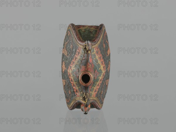 Waterskin matara, Turkish, Ottoman dynasty 1299–1922, 2nd half of the 16th century, Turkey, vessel; leather, kidney-shaped waterskin with an appliqué of a colorful lizard; height 23.0 cm, width 24.5 cm, depth 14.0 cm, weight 0.62 kg. Bottle with rounded bottom, narrow neck for pouring and a small spout for drinking; decorated with applied arabesques cut from shagreen and arabesques painted with gold. One narrow side bears a protective emblem in the form of a six-pointed star Seal of Solomon intended to ensure the water's freshness. The leather matara is a copy of gold bottles set with precious stones used at the sultan's court and may have been used by the sultan during military expeditions in Europe. The matara is a unique object type; four such artifacts are known worldwide., An ornate object with a symmetrical, elongated shape sits against a plain pale gray background; the object displays a textured surface with decorative patterns in shades of green, red, orange, gold, and dark gra...