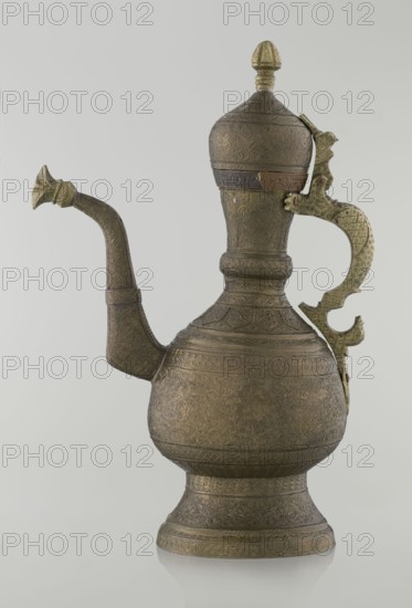 Jug aftabe, Persian, Qajar dynasty 1785–1925, aftabe vessel in ceramic, 19th century, possibly Central Asia or Iran. Decoration: dense plant and geometric ornament, dragons, zoomorphism; geometric and plant ornament. Height 34.0 cm, width 22.7 cm, diameter 13.3 cm., A metal pitcher with an elongated curved spout and a decorative handle stands against a light gray background, showing a patinated surface in shades of brown, bronze, and muted gold. The vessel has a bulbous lower body tapering into a narrower neck topped with a domed lid and finial, all covered in intricate engraved floral and geometric patterns. The spout is slender and ornate with a flared tip, and the handle is sculpted with a textured, lattice-like design and a hinged attachment near the lid. The base flares outward with repeating engraved bands, and the overall object shows subtle variations in tone where the metal has aged, combining darker brown areas with brighter golden highlights.