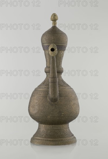 Jug aftabe, Islamic art, Persian, Qajar dynasty 1785–1925; aftabe with dense plant and geometric ornament, dragons, zoomorphism; 19th century, origin: possibly Central Asia, Iran; vessel; height 34.0 cm, width 22.7 cm, diameter 13.3 cm., An ornate metal vessel with a rounded base and a tall, narrowing neck topped by a domed lid with a pointed finial, featuring a long curved spout extending from the neck; the surface is covered in intricate engraved patterns and decorative bands, and the visible colors are various shades of brown and brass with hints of darker brown and muted gold against a pale gray background.